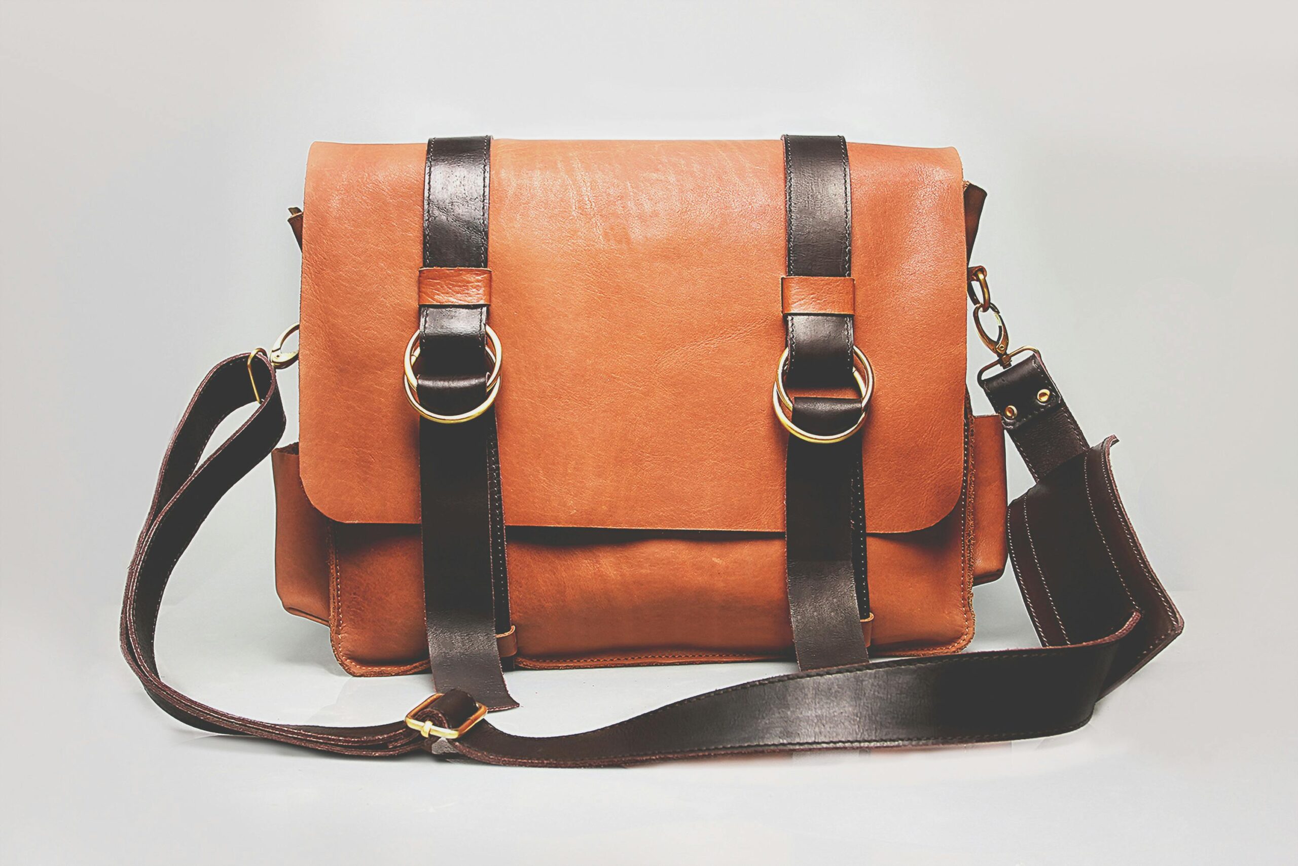 Elegant brown leather briefcase with dark straps and metal buckles, ideal for fashion and business.